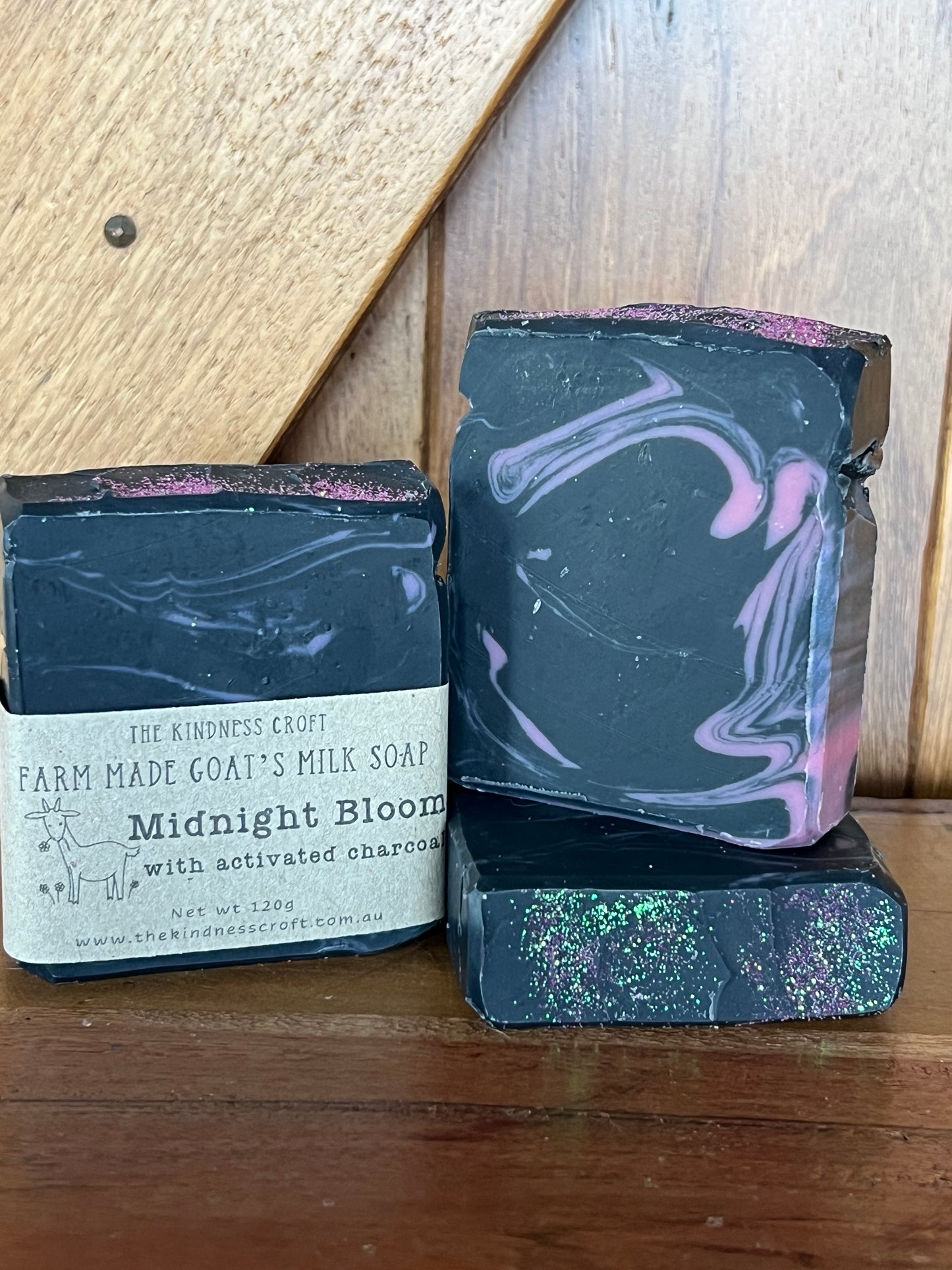 Three bars of slack and pink swirled soap with a label on a wooden surface