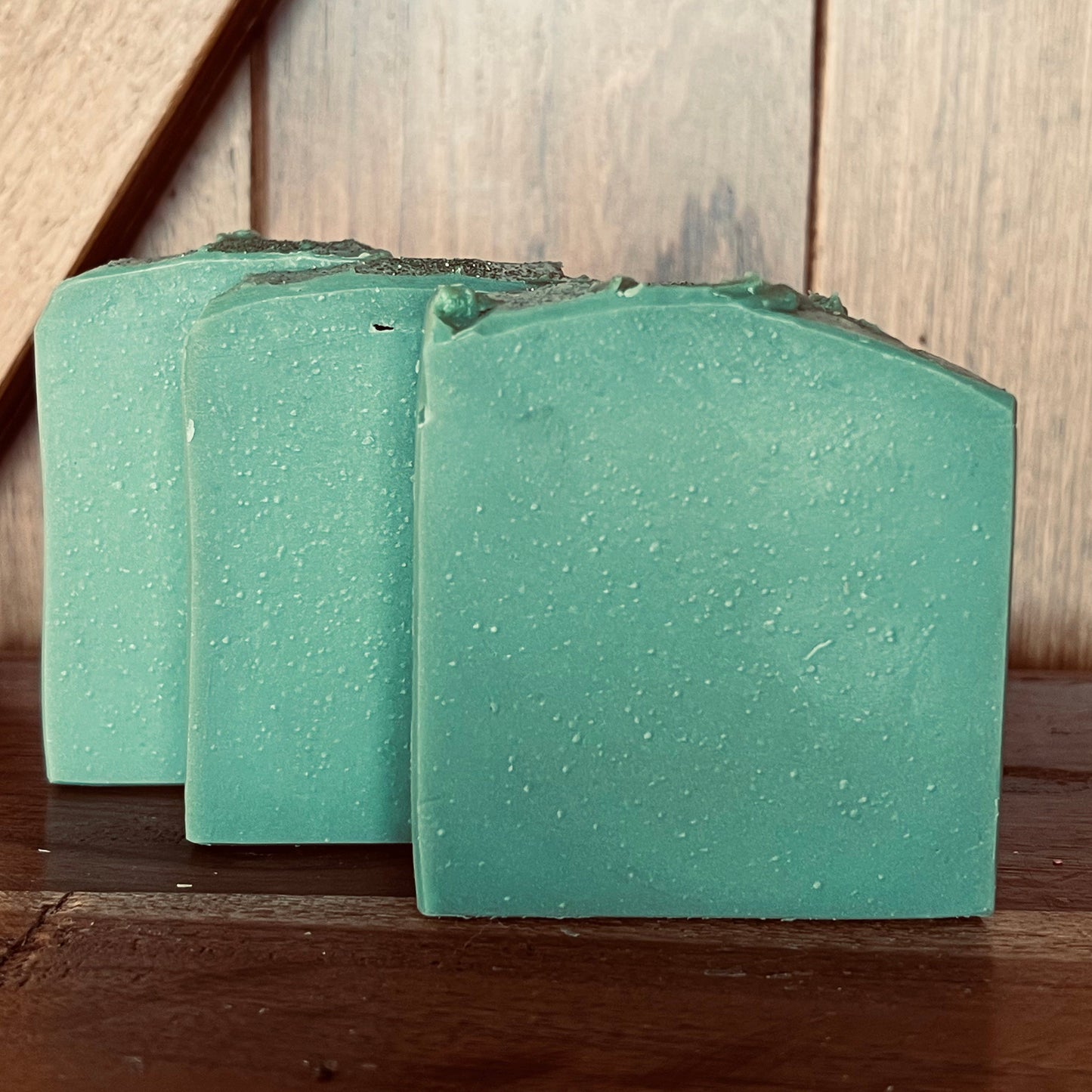 Three green bars of soap on a wooden surface with a wooden background