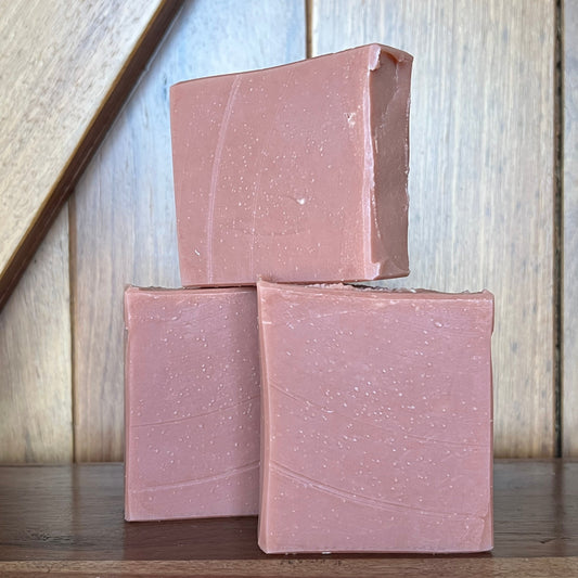 Three pink soap bars on a wooden surface