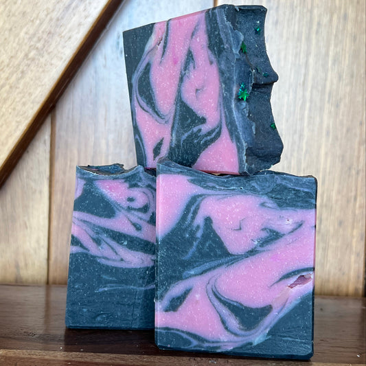 Three bars of soap with pink and black marbled pattern on a wooden surface