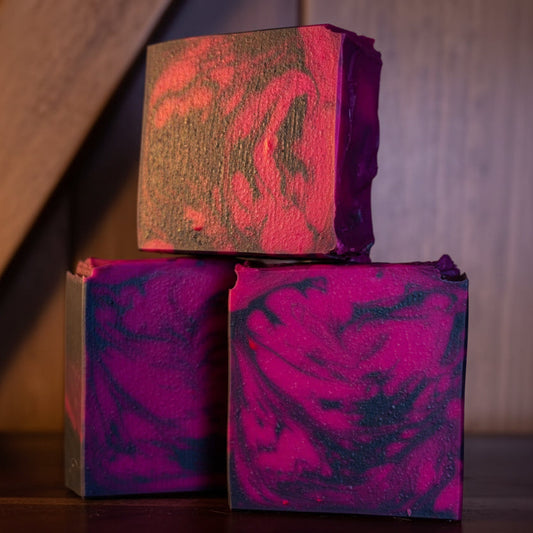 Three bars of pink and black marbled soap on a wooden surface