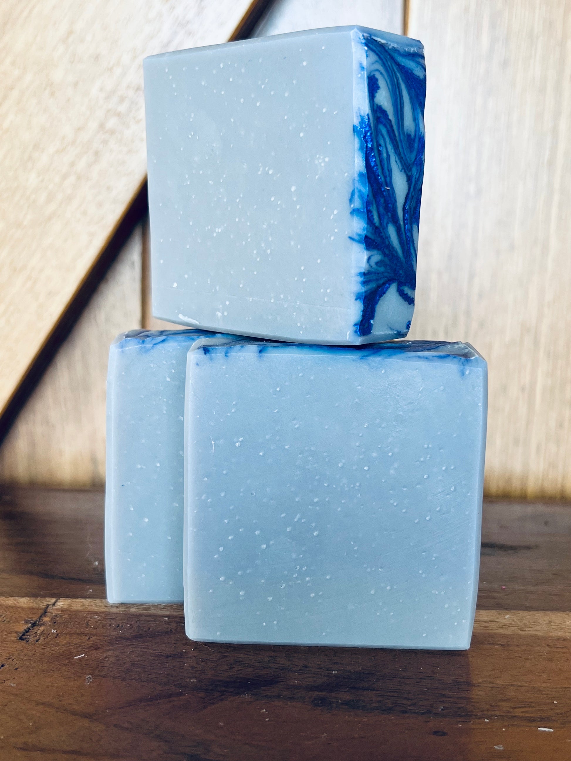 Two blue and white marbled soap bars stacked on a wooden surface with a neutral background.