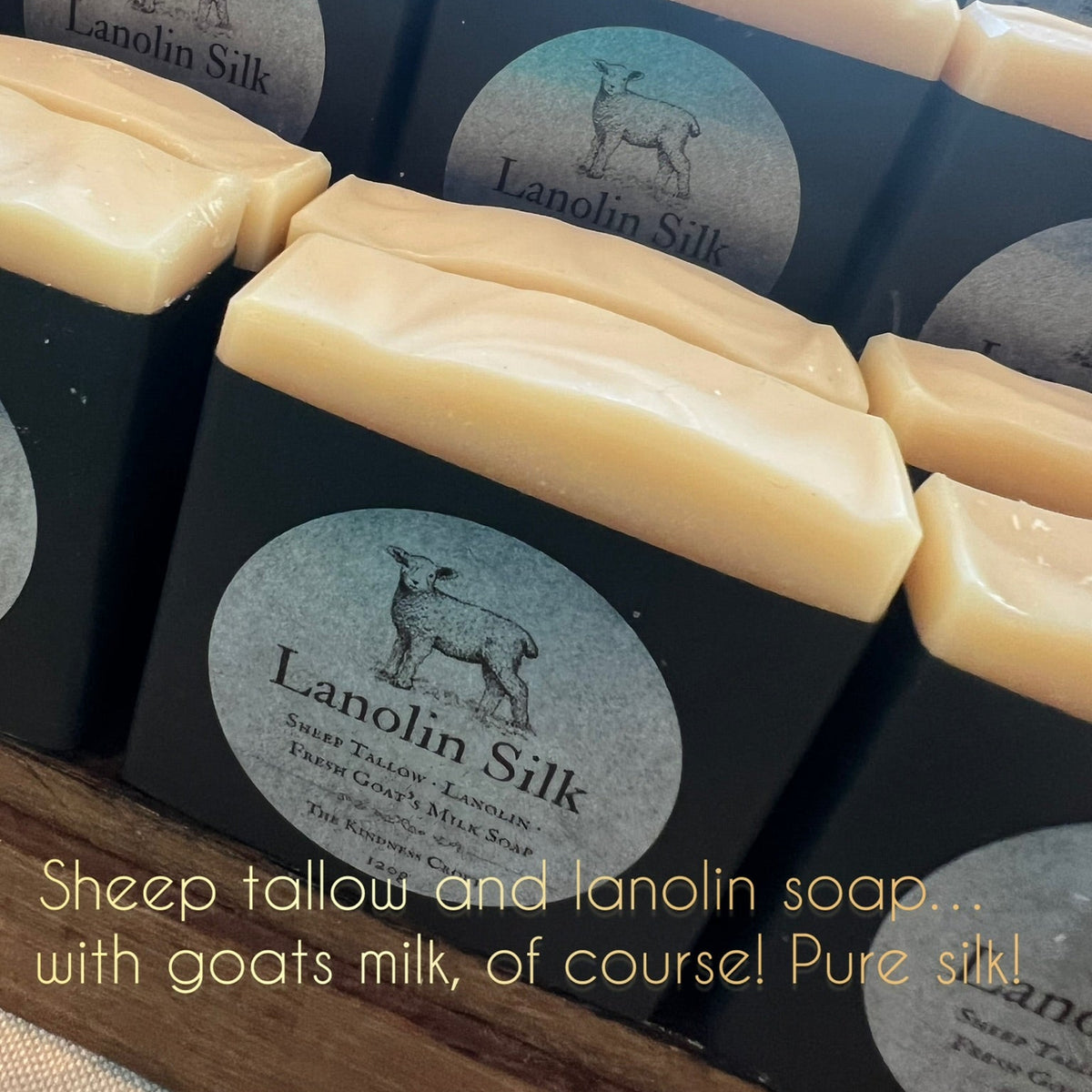 Several bars of Lanolin Silk soap in pale cream-colored wax are arranged in a display, each in a black box with a round silver label showing a deer silhouette and the brand name Lanolin Silk. A text overlay at the bottom reads: 'Sheep tallow and lanolin soap.